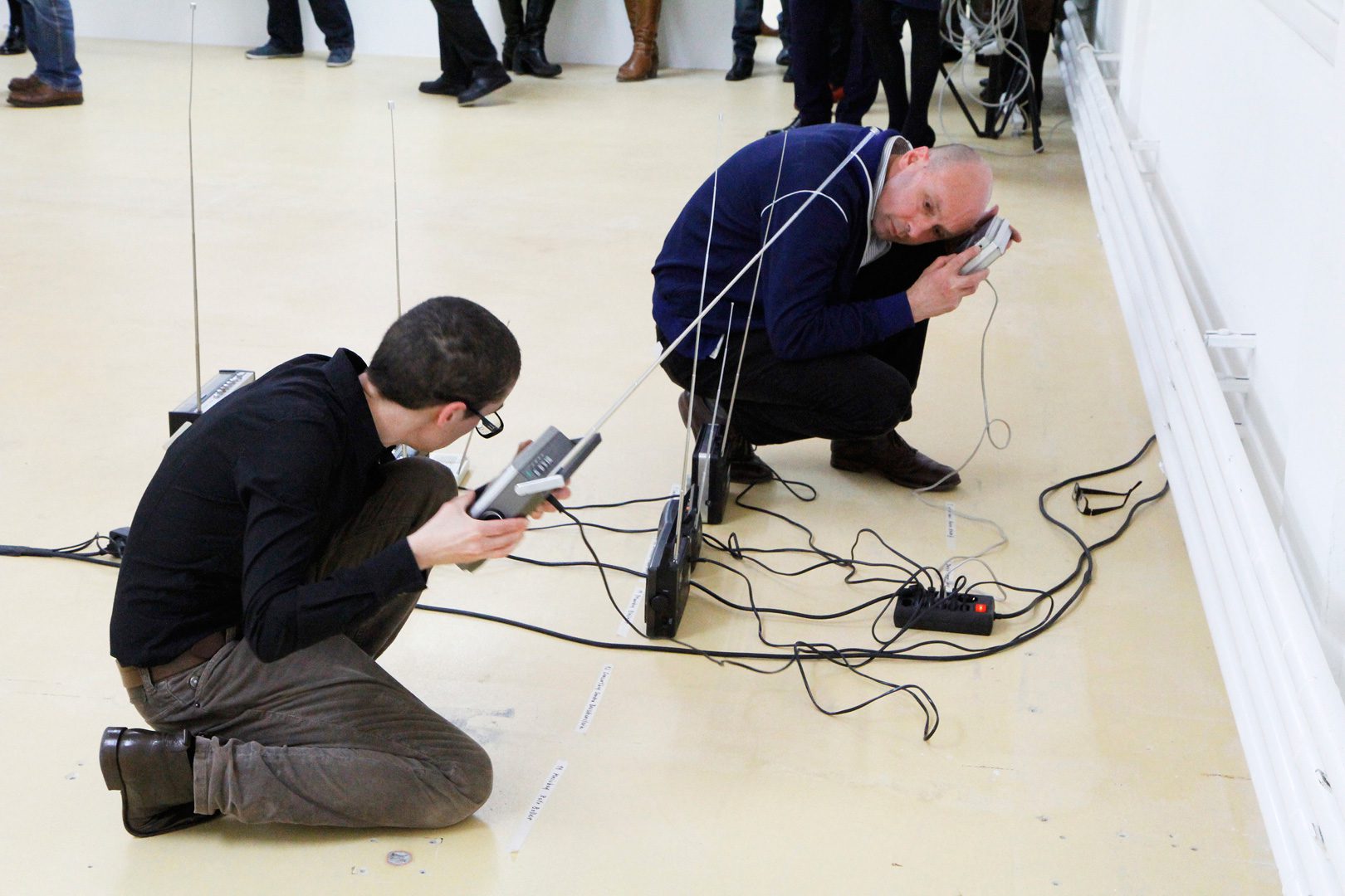 zwei Personen lauschen am Boden hockend nach alten Radiogeräten